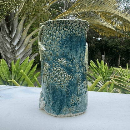 Blue ceramic vase with turtle design on a white surface with greenery in the background
