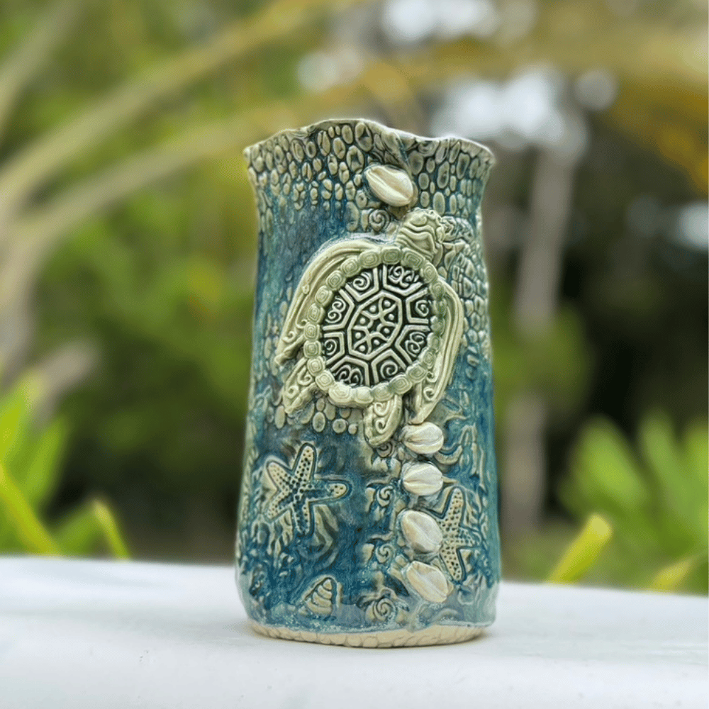 Ceramic vase with turtle design against a blurred green background