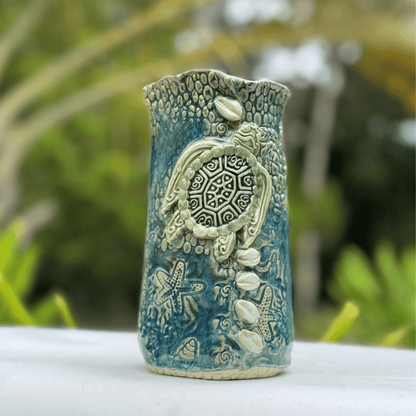 Ceramic vase with turtle design against a blurred green background