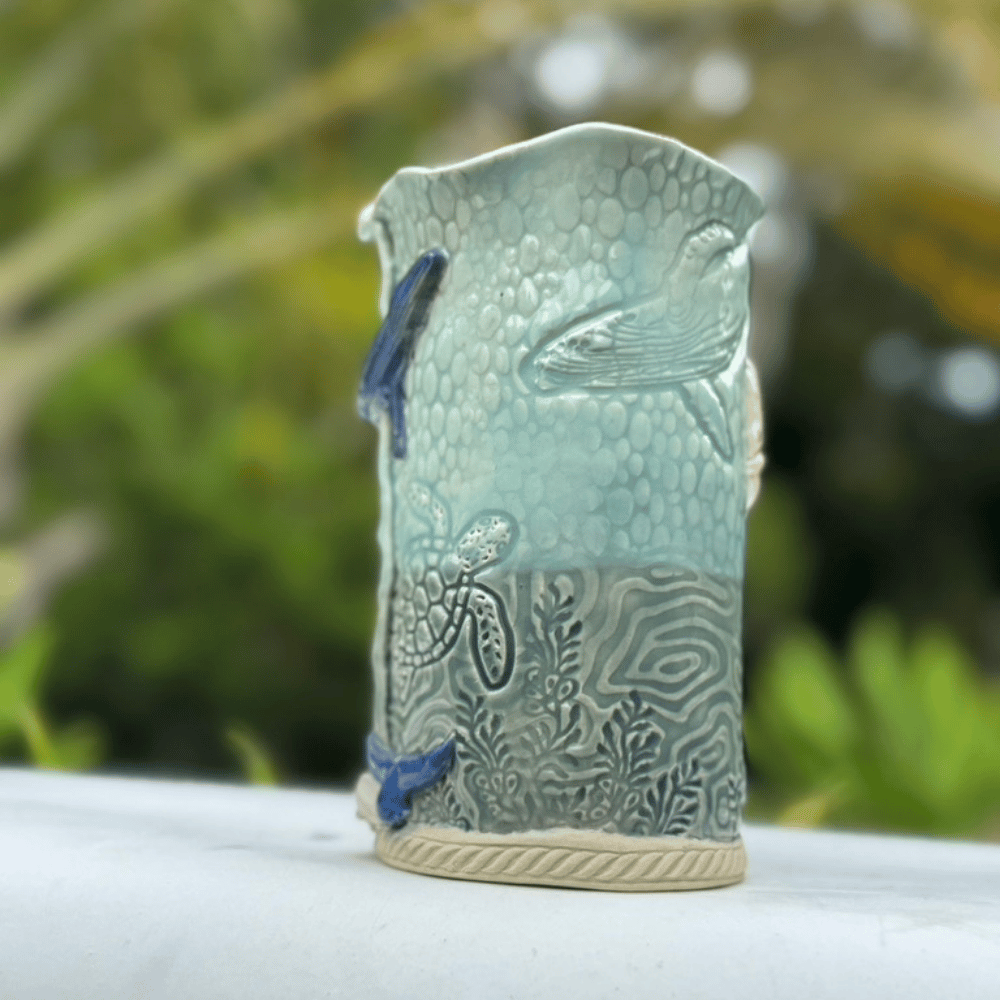 Ceramic vase with fish designs on a white surface with a blurred green background