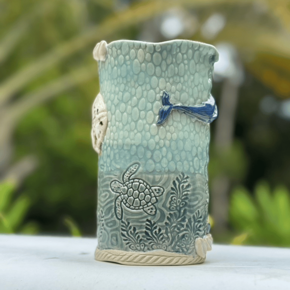 Ceramic vase with ocean-themed design featuring a turtle and fish, set against a blurred natural background.