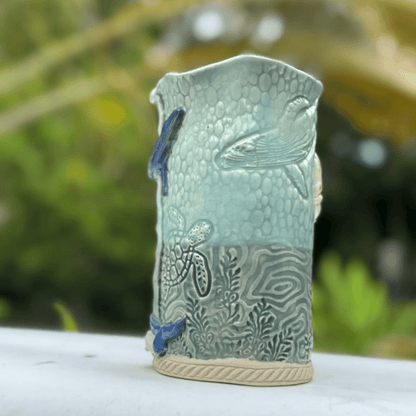 Decorative ceramic vase with fish and wave patterns on a blurred natural background