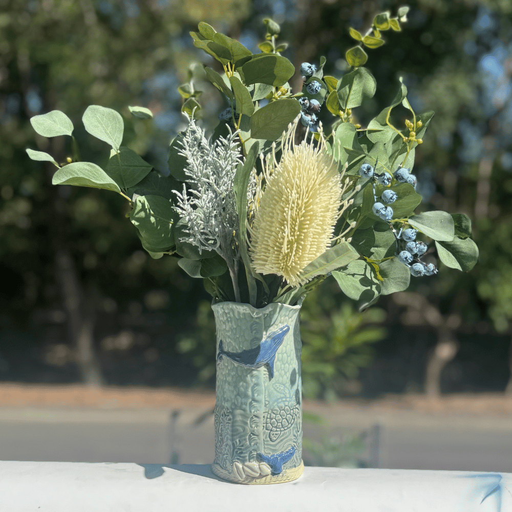Decorative whale vase with a floral arrangement against a blurred natural background