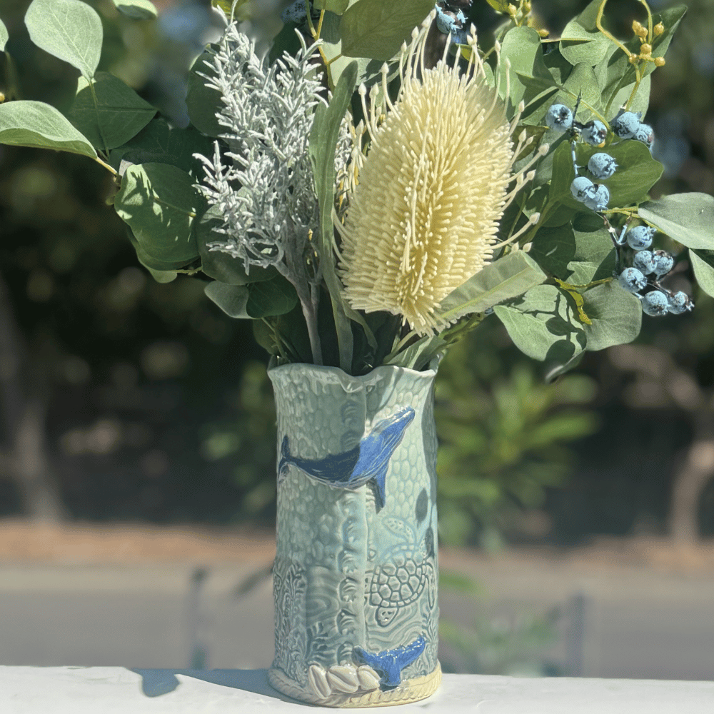 Decorative whale and shell vase with floral arrangement on a blurred natural background