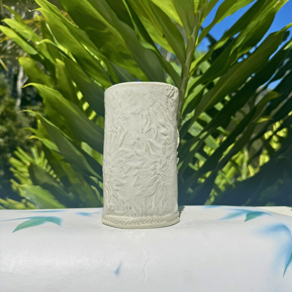 Textured ceramic vase on a surface with green foliage in the background