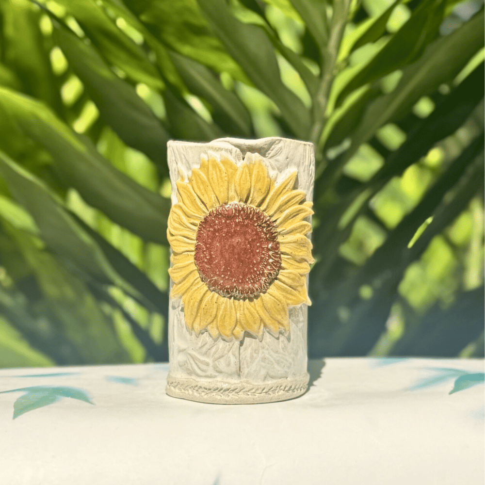 Decorative vase with sunflower design on a surface with green foliage in the background