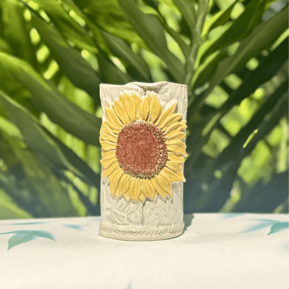 Decorative vase with sunflower design on a surface with green foliage in the background