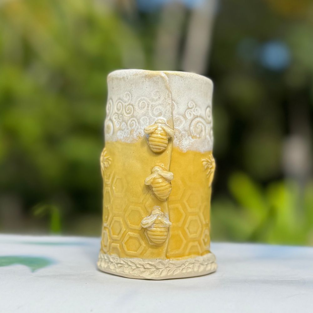 Ceramic bud vase with bee and honeycomb design on a blurred natural background