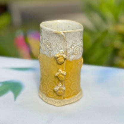 Ceramic bud vase with bee and honeycomb design on a blurred natural background